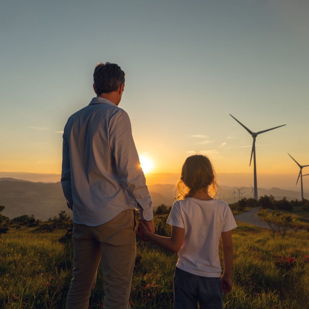 WIndkraftanlagen mit Sonnenaufgang, Vater mit Tochter im Vordergrund